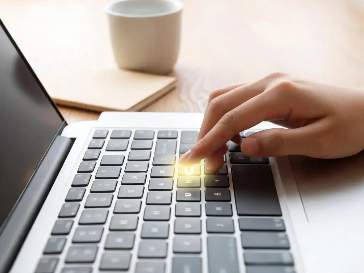 Palec unosi się nad klawiszem „u” na klawiaturze laptopa, podkreślając wpisywanie znaku ü w przytulnym miejscu pracy.