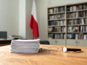 Smartfon z otwartym czatem i emotikonami w dłoni użytkownika, na biurku obok laptopa i kawy w przytulnym wnętrzu.